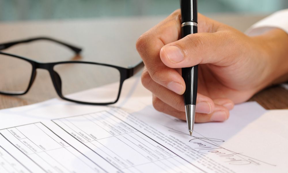 firma de un documento legal con un bolígrafo junto a unas gafas, relacionado con servicios de notary public