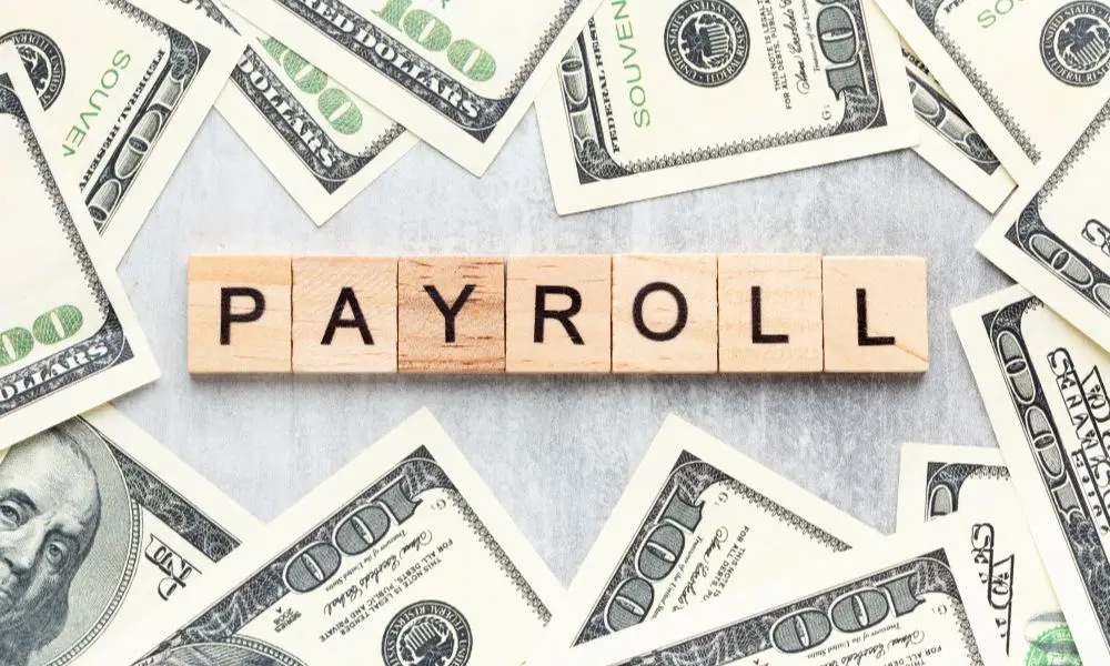 Bloques con la palabra payroll rodeados de billetes de dólar, representando servicios de contabilidad y payroll.